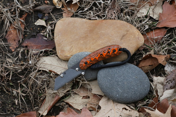 Banzelcroft Customs MEK, a titanium EDC utility knife with orange and black G10 handle scales.